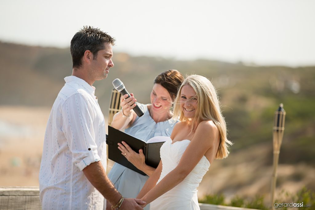 Groom speaking into female celebrants microphone while bride looks at guests and laughs