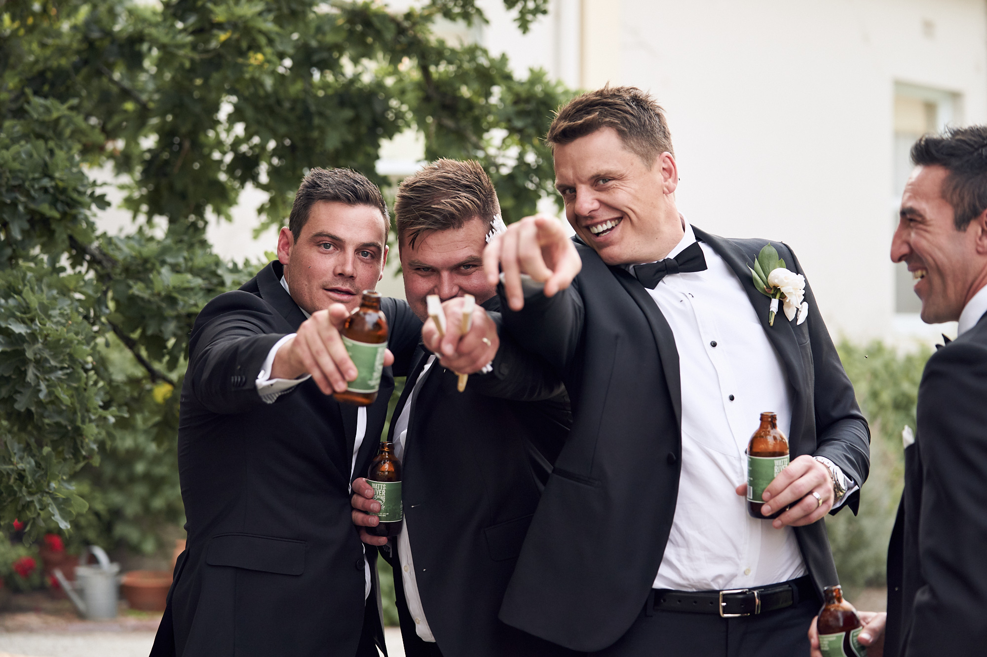 Groom and groomsmen holding drinks laughing and pointing to camera