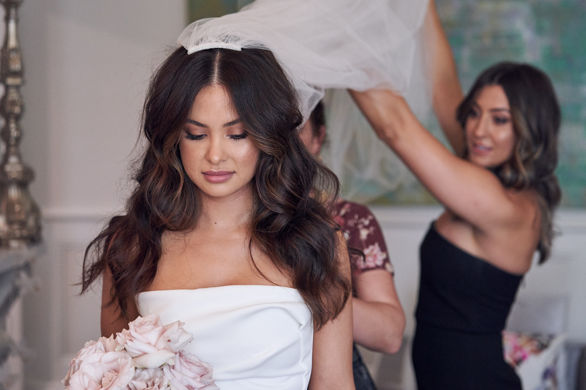 Bridesmaid helping bride put her veil on 