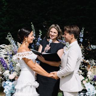 Celebrant holding microphone, smiling at bride and groom during marriage ceremony