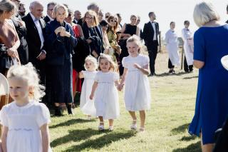 4 flowergirls dressed in white walking down the aisle at wedding