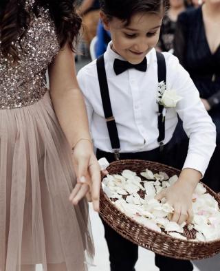 Young boy reaching into a basket of flower petals as he walks down the aisle at wedding
