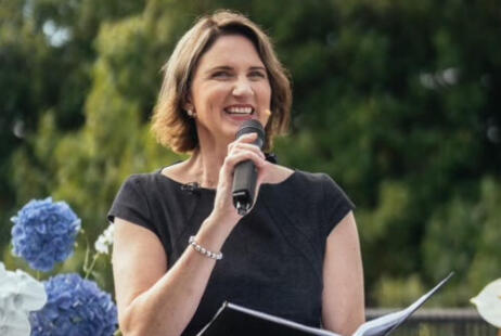 Female marriage celebrant smiling and talking into microphone during outdoor wedding ceremony