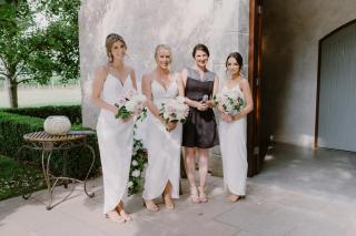 Three bridesmaids in white and wedding celebrant in dark grey, standing together outside wedding chapel at Stones of the Yarra Valley